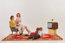 A retro-styled family of four, including two children, gathers on a rug, watching a vintage television. It evokes a cozy, domestic scene.