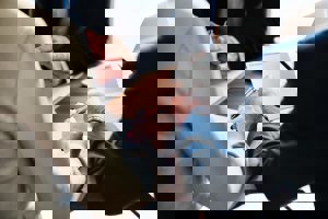 Three people are gathered at a table, engaged in a discussion over documents. One person writes with a pen while another points, suggesting a collaborative meeting or agreement.