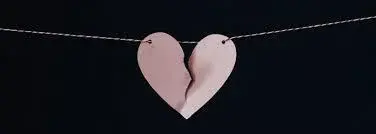 A two-part pink heart hangs from a string against a dark background. The heart, split down the middle, is rejoining, symbolizing resolution or healing.