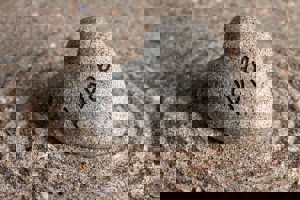 A heart-shaped stone engraved with "Hope" rests on rippled sand. Concentric circles surround the stone, creating a serene, Zen-like image.