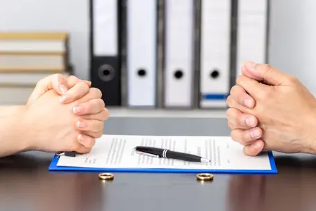 Two people sitting across from each other with signed document and wedding rings in the middle