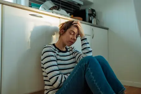 Stressed woman sitting on her kitchen floor