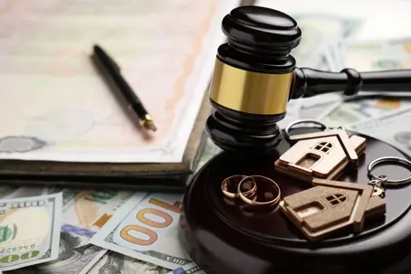Gold wedding rings, wooden house model, and a judge gavel on legal paperwork