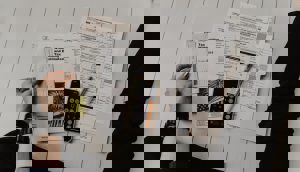 A person's hands review tax forms including "U.S. Individual Income Tax Return" and "Estimated Tax for Individuals," with a phone and calculator on a light floor.