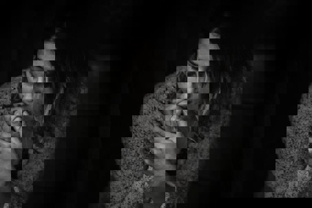 A black and white image of a woman looking down, biting her fingers. She appears distressed, reflecting the impact of harassment.